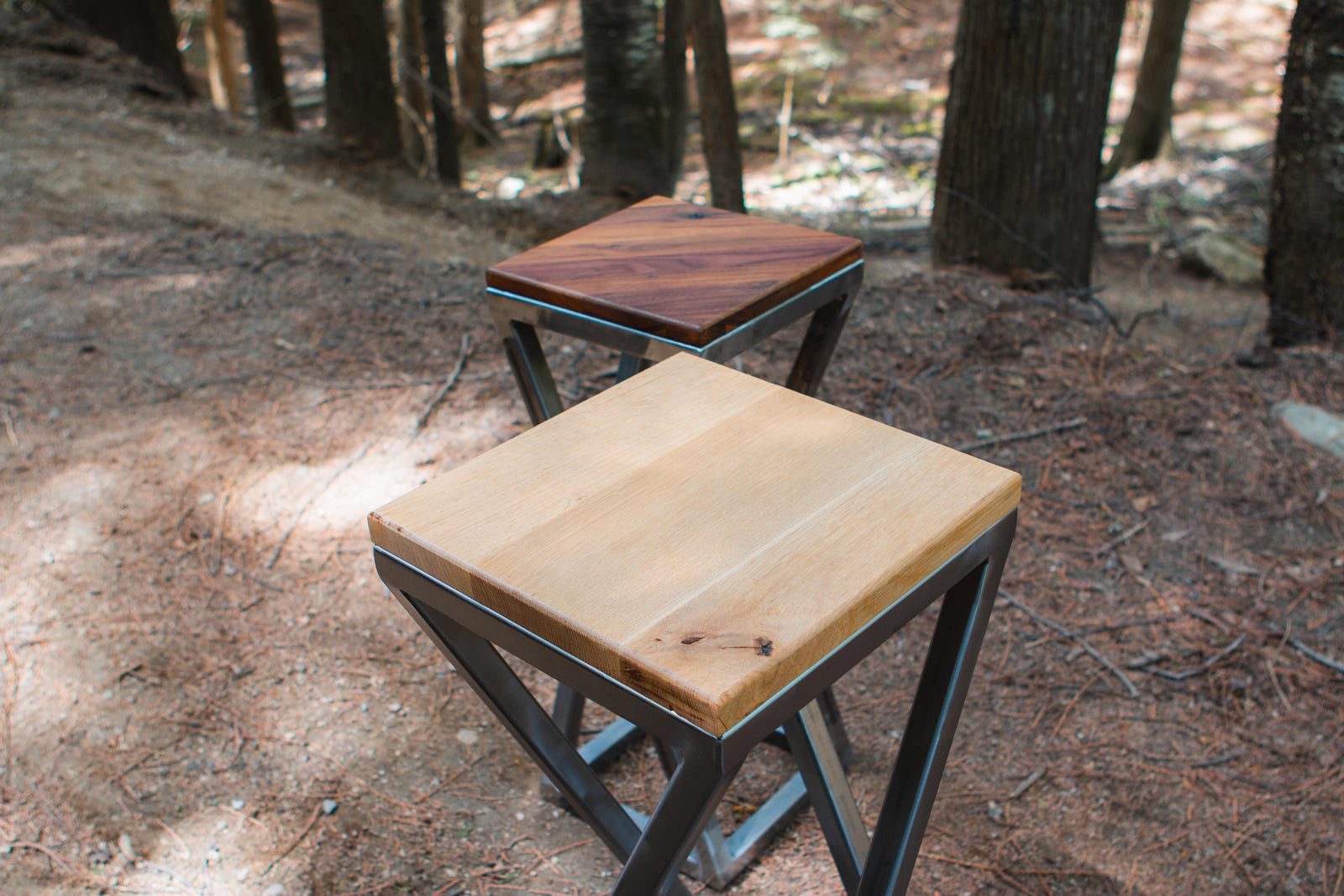 Two wooden stools with metal legs in a forest setting