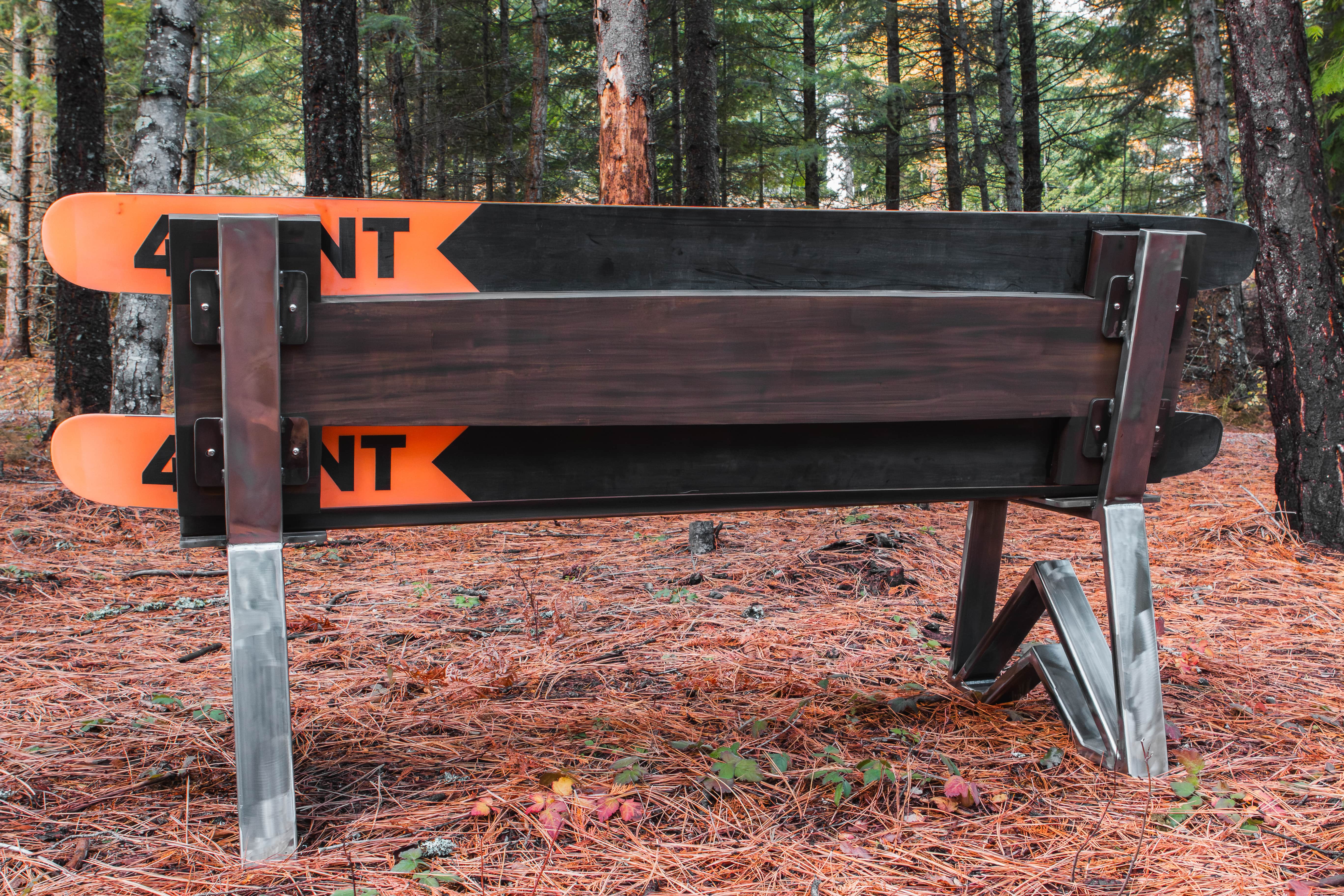 Wooden bench with orange and black skis in a forest setting