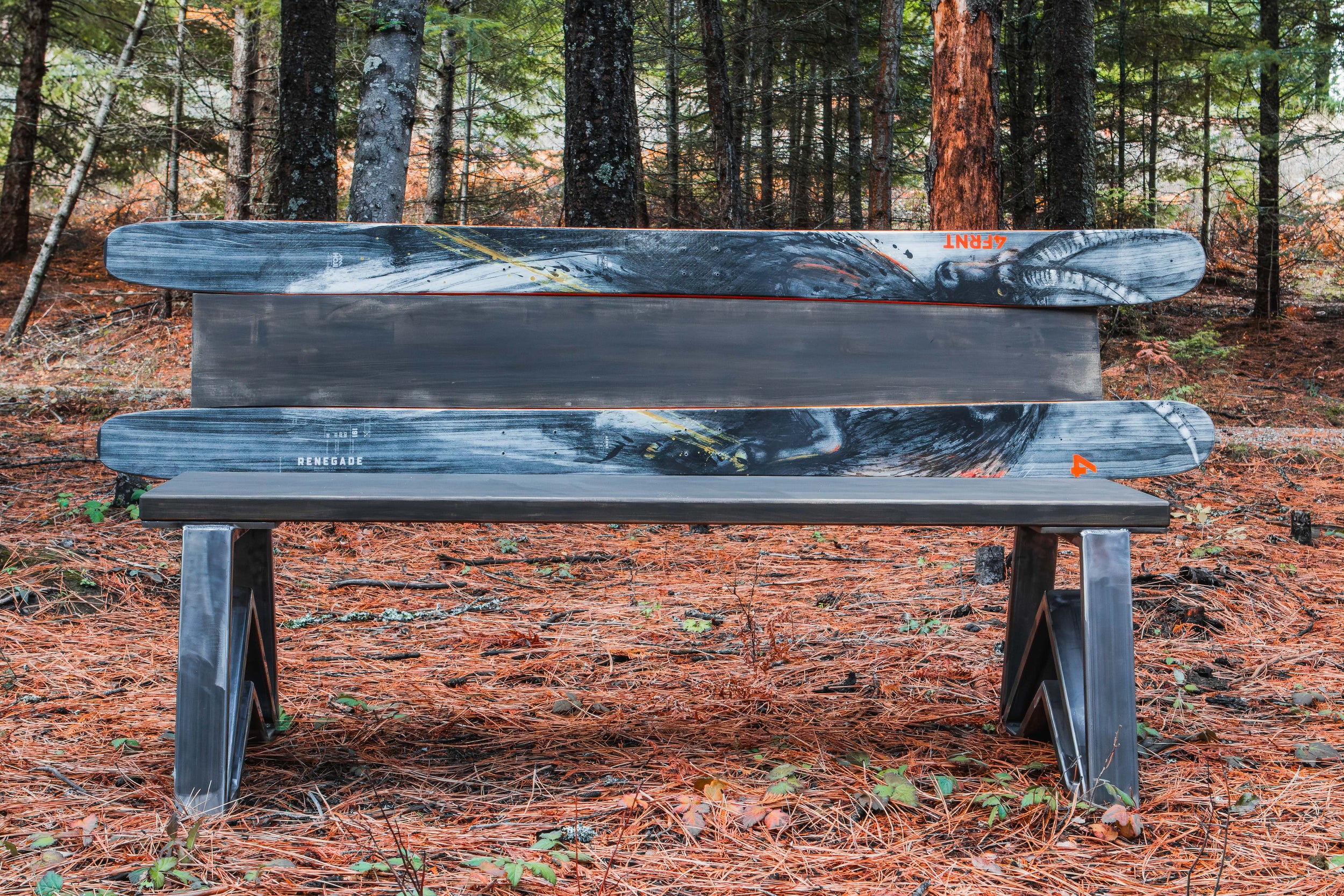 Wooden bench in a forest setting with trees and fallen leaves in the background.