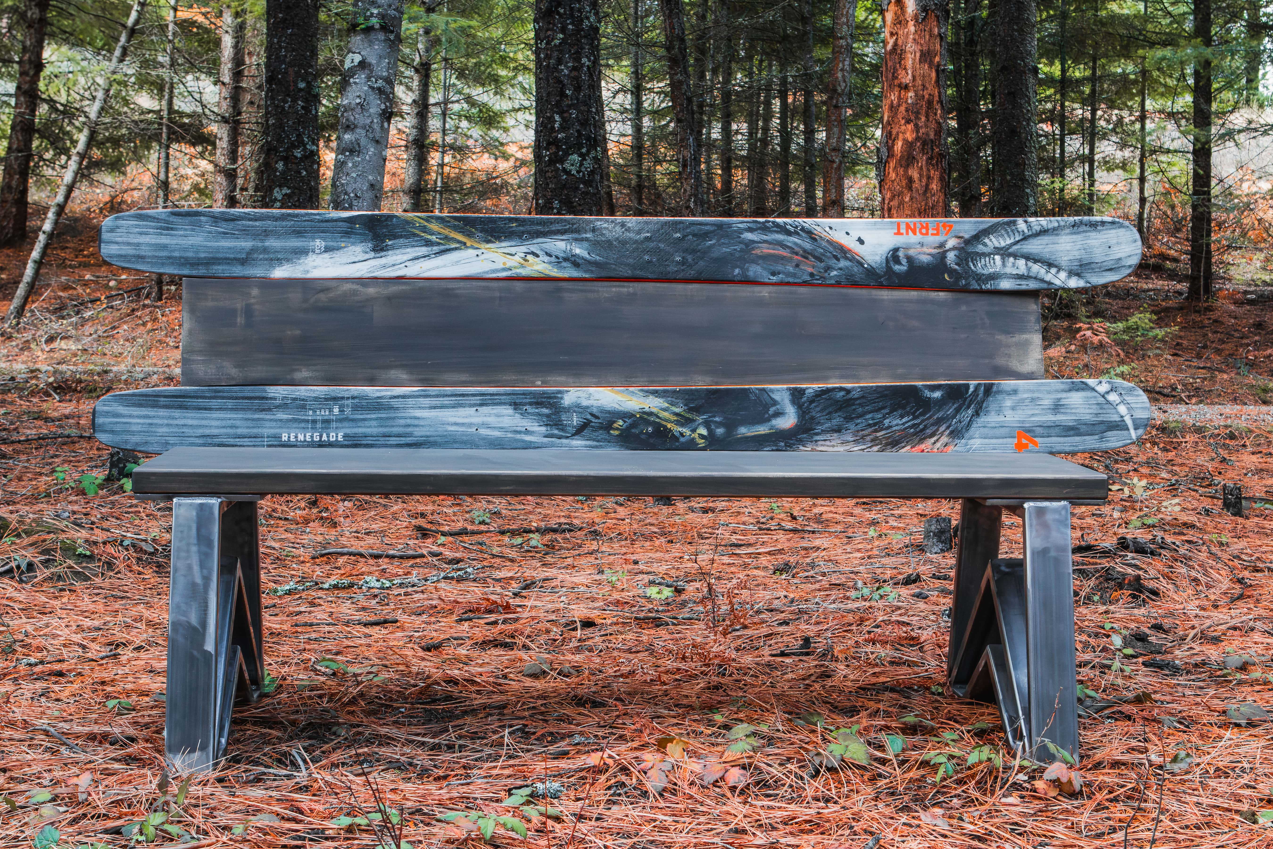 Wooden bench in a forest setting with trees and fallen leaves in the background.