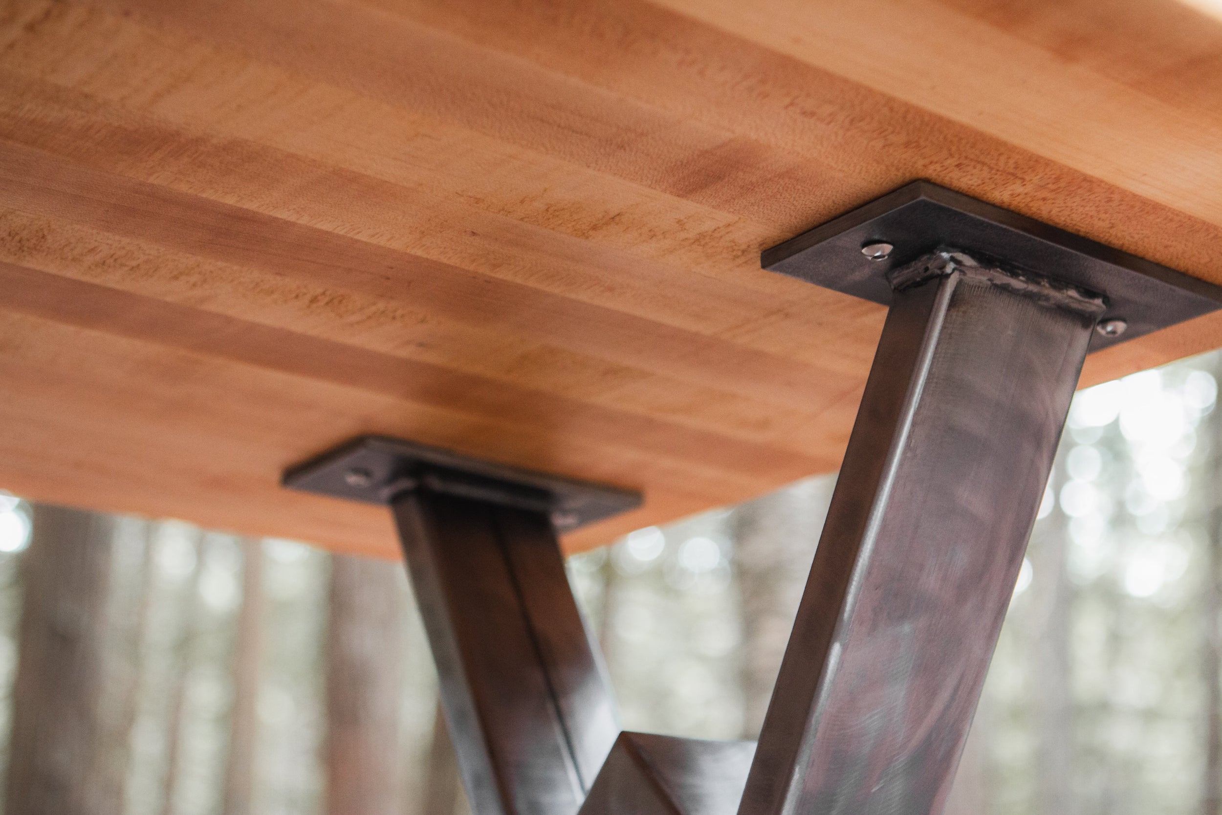 Wooden table with metal legs against a blurred forest background