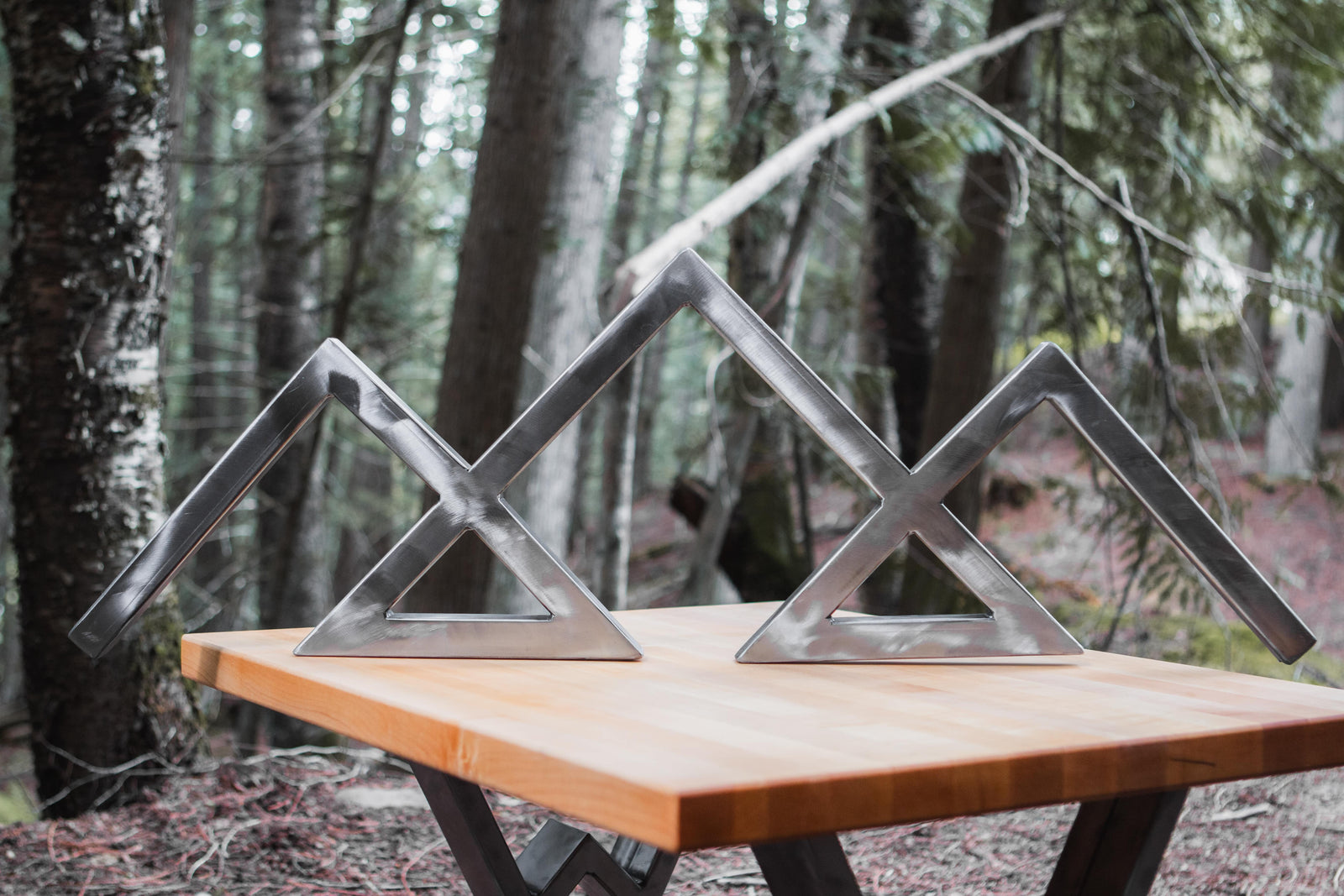 Metal mountain sculptures on a wooden table in a forest setting