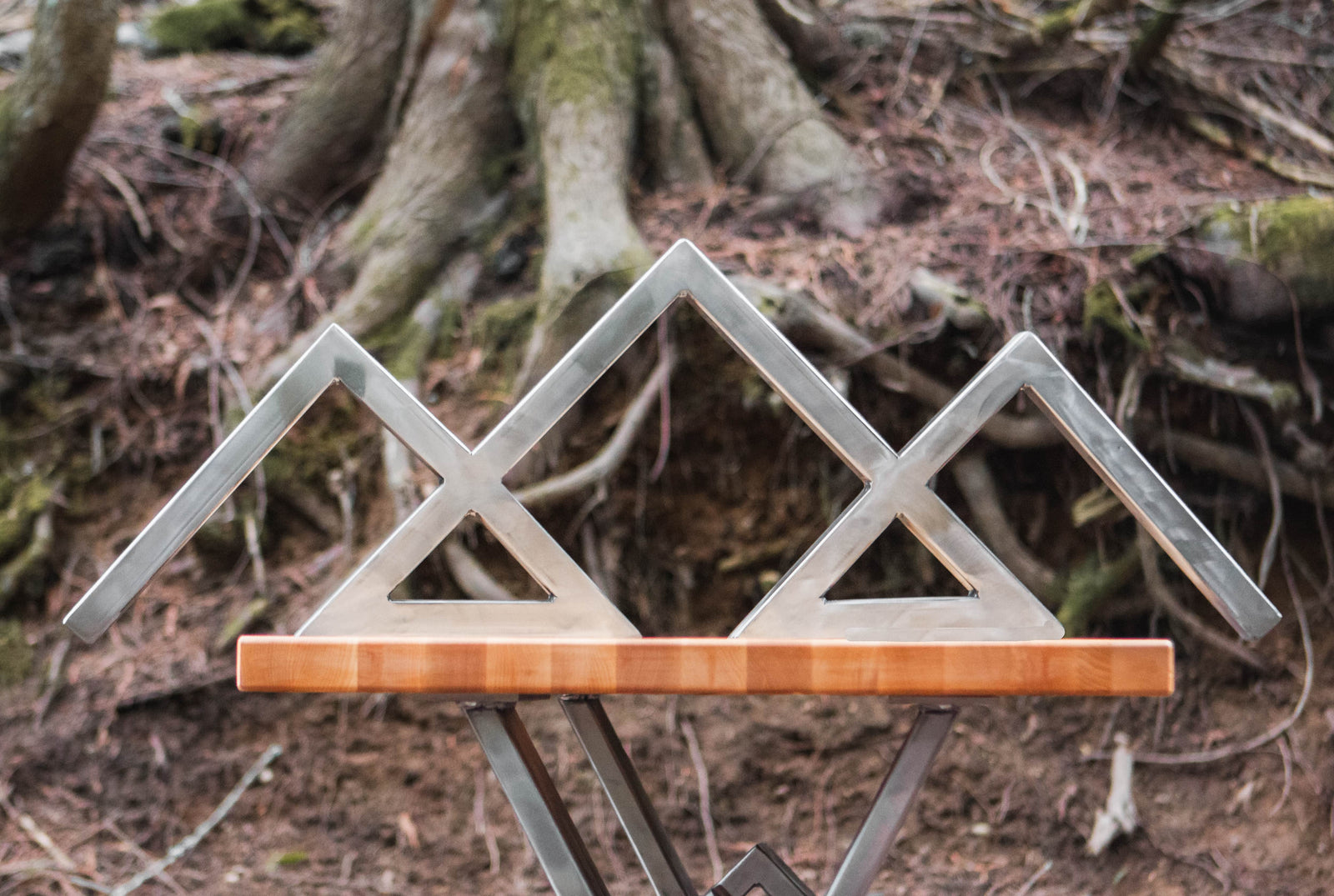 Wooden table with a metal mountain sculpture on a forest floor background