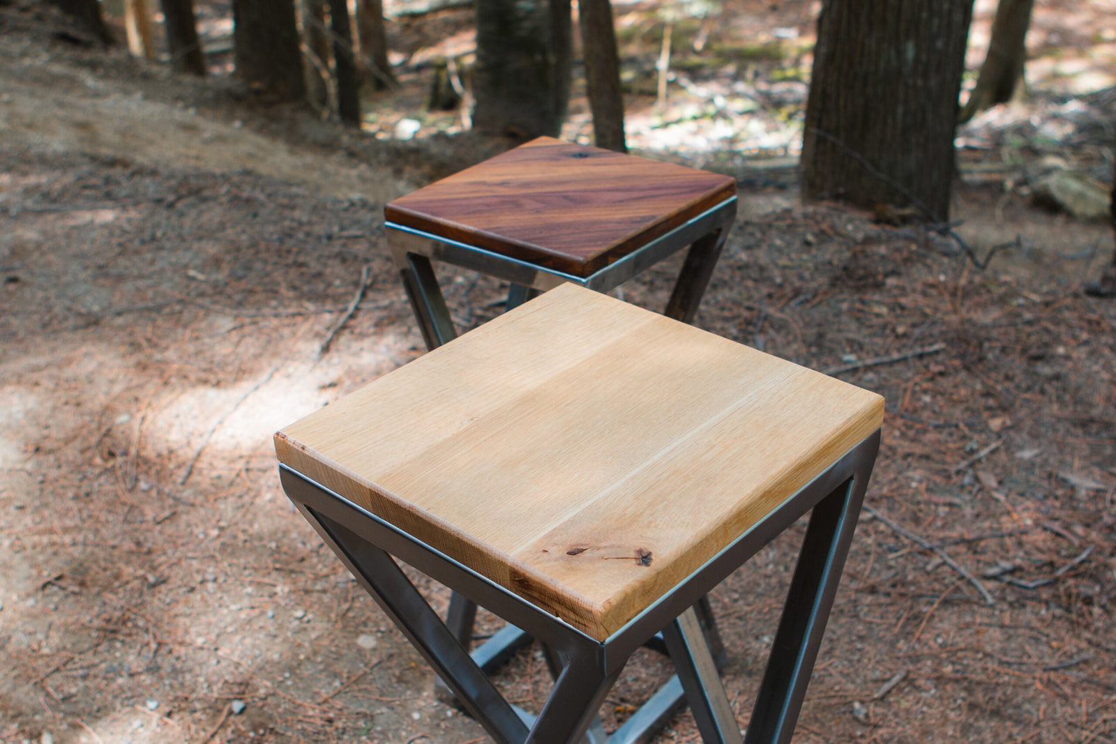 Two wooden stools with metal legs on a forest floor.