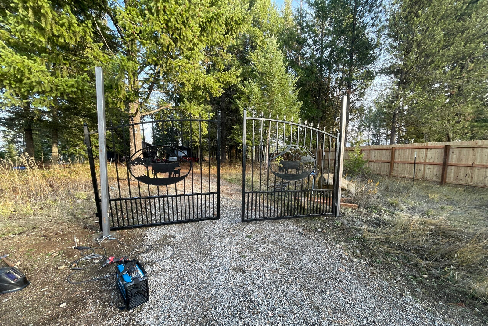 Metal gate in a wooded area with tools on the ground.