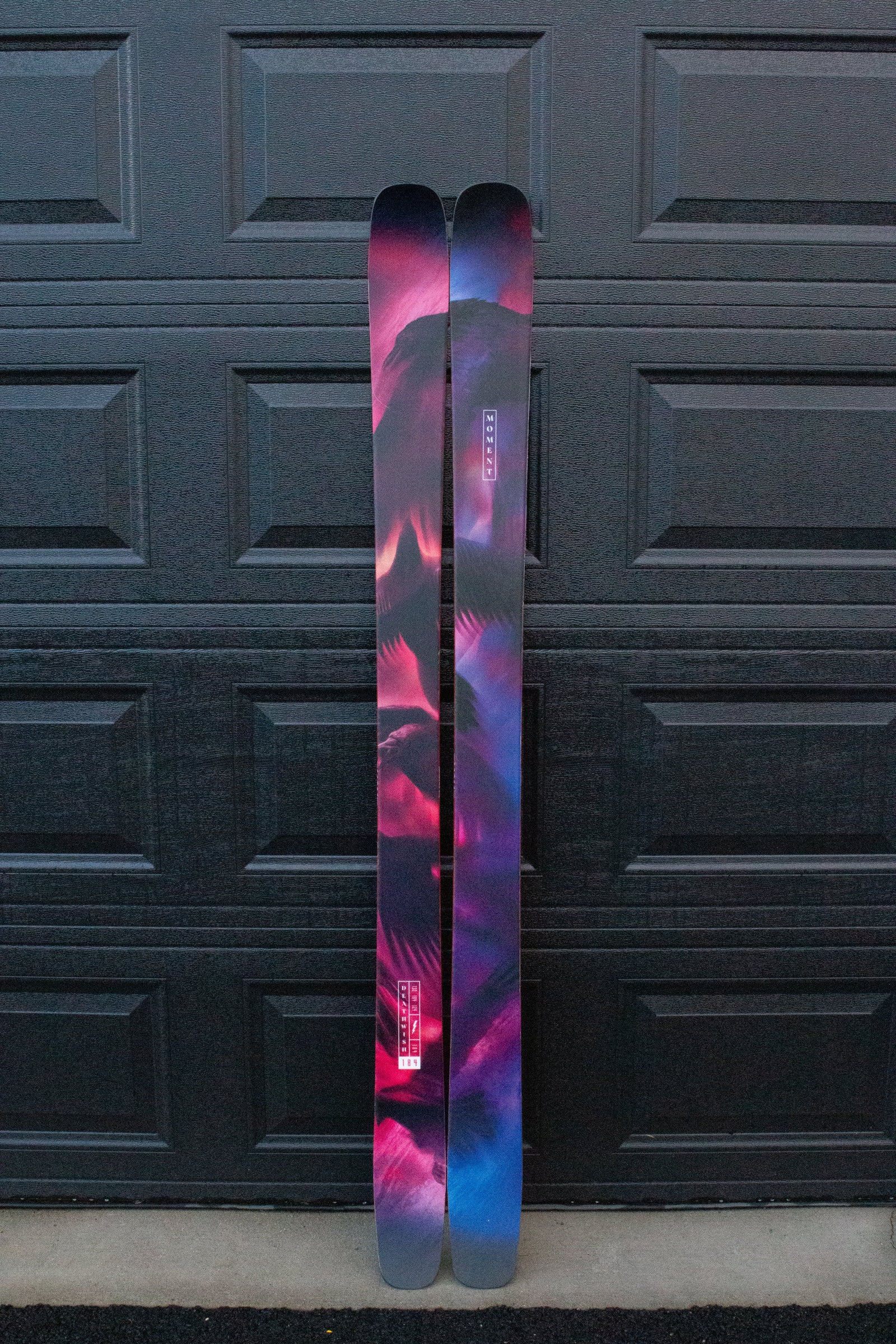 Two skis with a colorful design leaning against a dark textured wall.