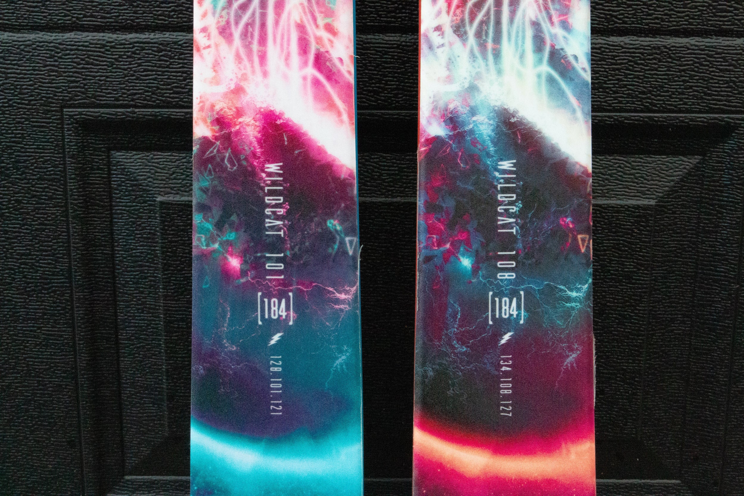 Two colorful snowboard decks with abstract designs on a black background