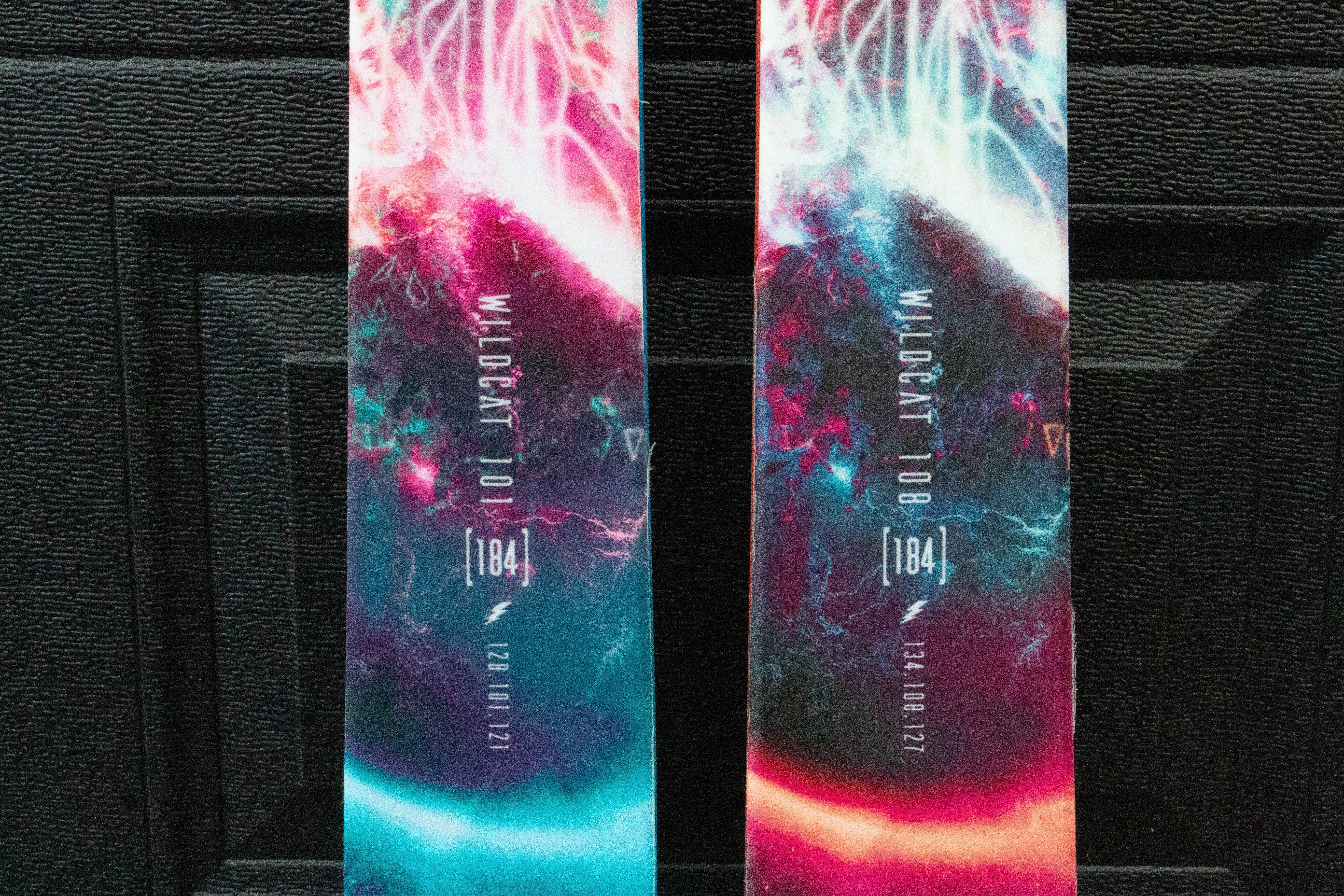 Two colorful snowboard decks with abstract designs on a black background